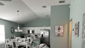 Una cocina moderna con armarios blancos, un refrigerador de acero inoxidable y un comedor con un sofá gris y sillas blancas.