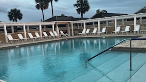 Una piscina con sillones blancos y una zona techada.