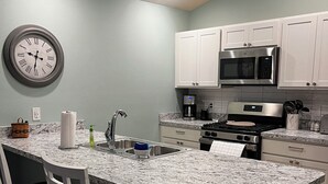 Una cocina con encimera de granito, armarios blancos, microondas de acero inoxidable y estufa a gas.