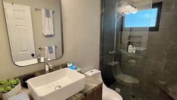 Een moderne badkamer met een grote spiegel, wastafel, toilet en douchecabine met glazen wanden.