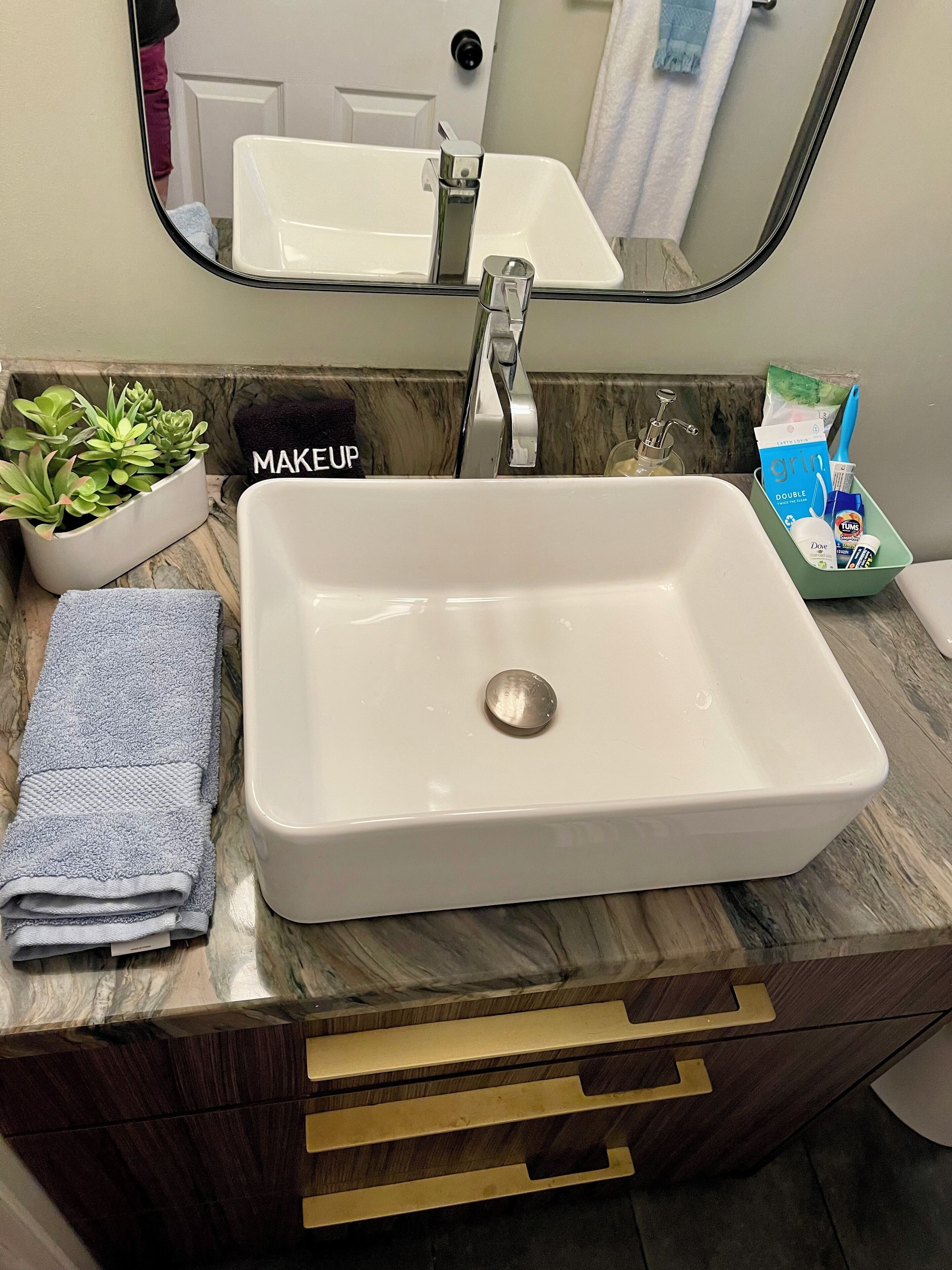 Een badkamer met een witte wastafel, een spiegel, een plant en toiletartikelen.