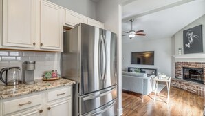 A kitchen with white cabinets, a stainless steel refrigerator, a coffee maker, and a marble countertop.