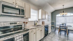 A kitchen with white cabinetry, a stainless steel stove, a microwave, and a dishwasher. There is a dining area with a round table and chairs.