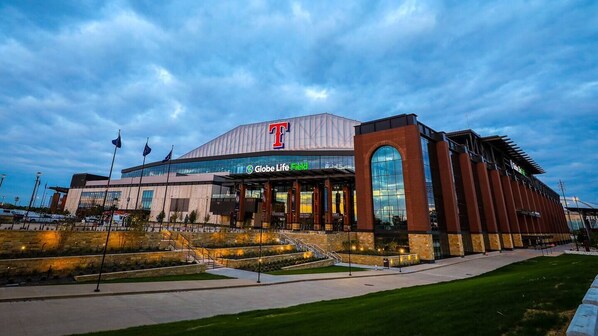 A large stadium with a prominent 'T' logo, a glass facade, and a sign reading 'Globe Life Field'.
