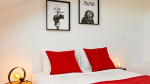 A bedroom with a bed, red pillows, a round table with a lamp, and two framed pictures on the wall. - Arroios Concept VI by Homing (Lisbon)