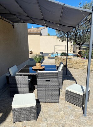 An outdoor patio with a table and chairs, a pool, and a covered area.