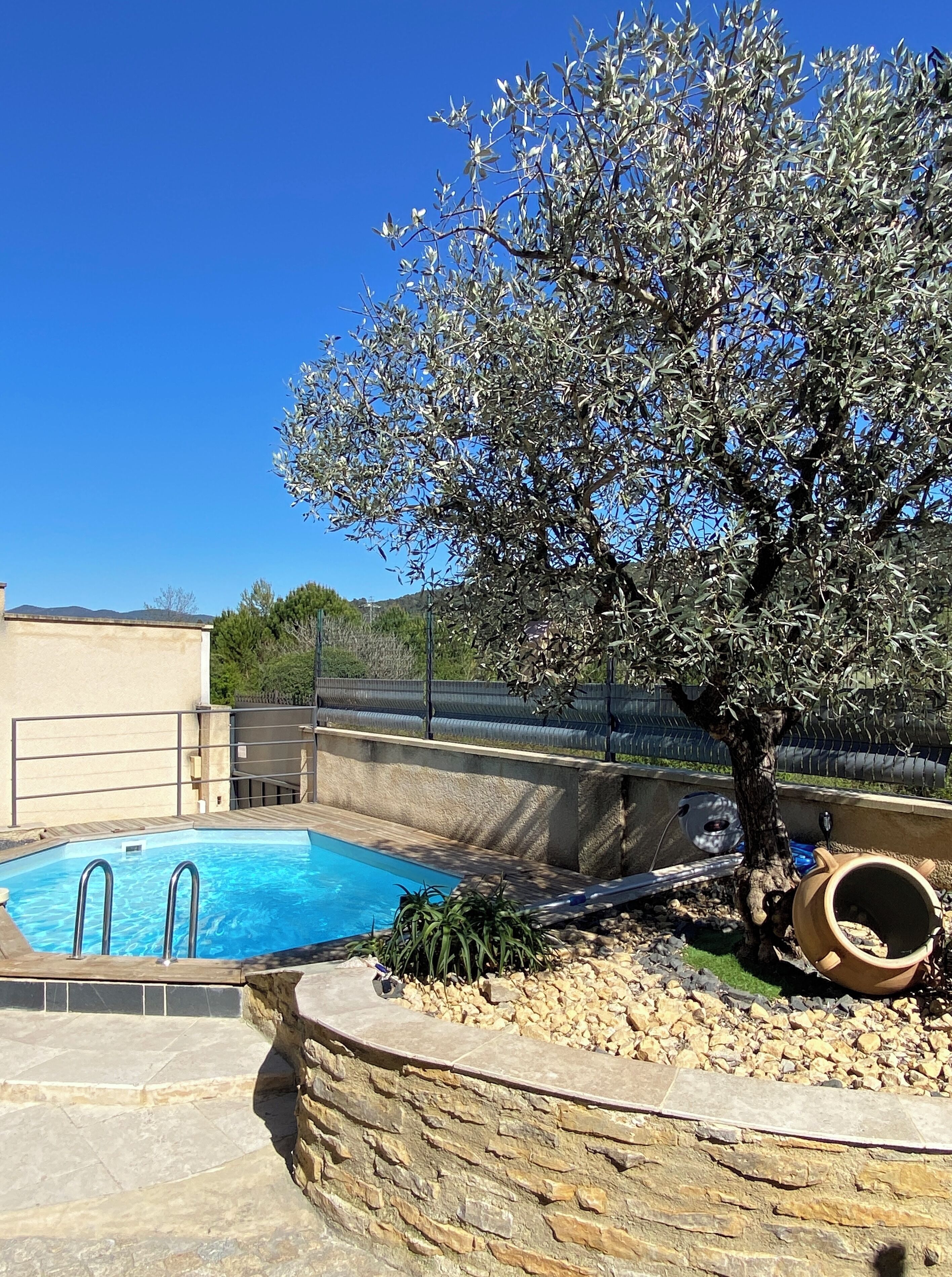A swimming pool with a stone wall, a tree, and a metal fence.