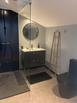 A modern bathroom with a glass shower enclosure, a round mirror, a sink with two handles, and a wooden ladder.