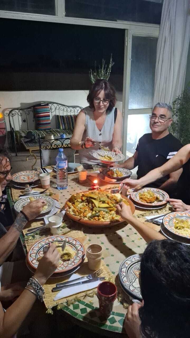 Un groupe de personnes est réuni autour d’une table, où se trouvent divers plats et une bouteille d’eau.