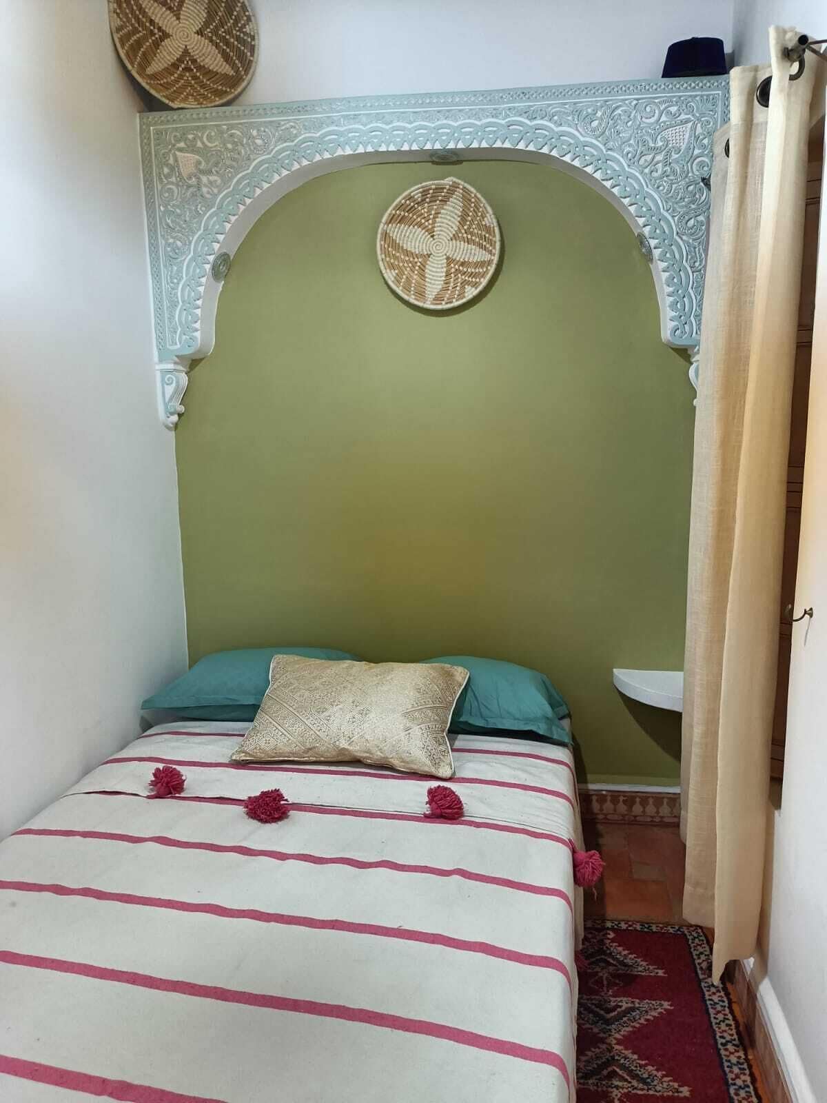 A small, cozy room with a bed, a decorative wall arch, and a small sink.