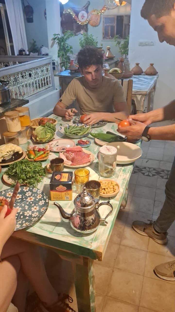 Een eettafel met verschillende gerechten en een theepot, omringd door mensen.