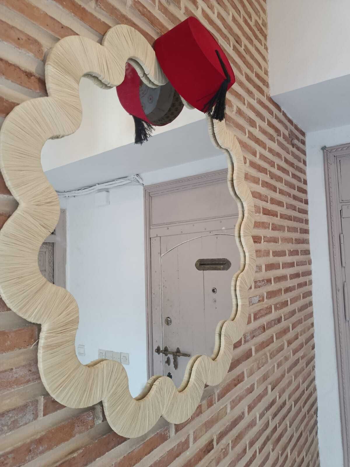 Espejo de marco ondulado que refleja una puerta y una pared de ladrillo.