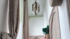 A hallway with a patterned rug, a small yellow table, and a hanging plant. - Dar Le Monde (Marrakech)