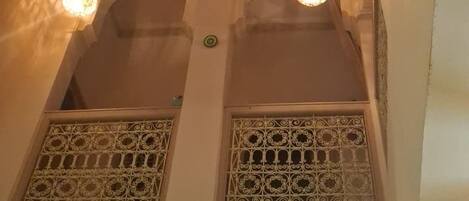 A room with a high ceiling, decorative ceiling fan, and two windows with intricate lattice designs.