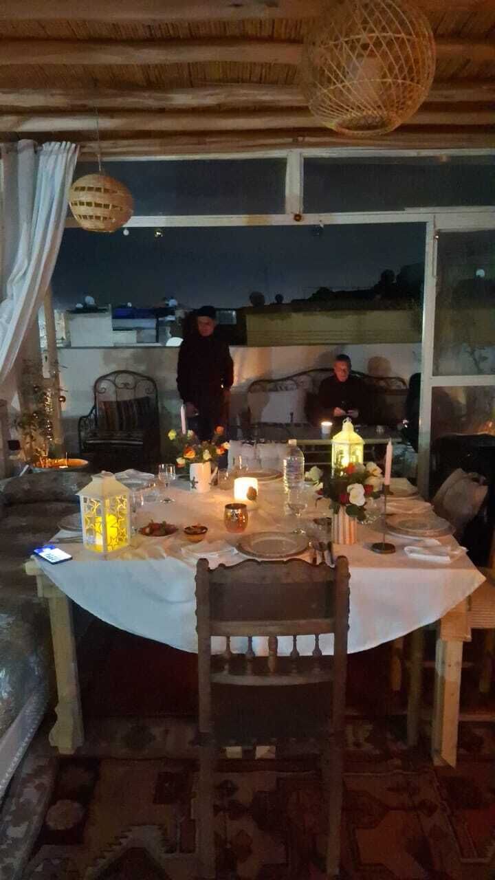 An outdoor dining area with a table set for two, a hanging light fixture, and a view of the cityscape at night.
