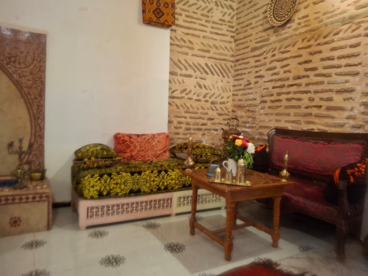 A room with a patterned wall, a sofa with a patterned cover, a small table with decorative items, and a patterned rug on the floor.