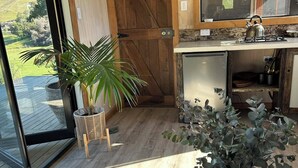 A room with a large window, a wooden door, a kitchen area, and a round table with a remote control.