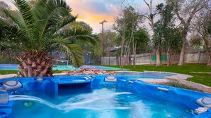 A hot tub area with a palm tree, surrounded by a wooden fence and a basketball court. - Pickleball & Heated Pool & Game Room & Mini Golf (San Antonio)