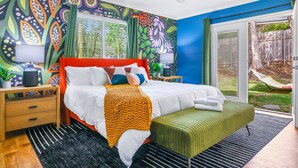 A modern bedroom with a bed, bedside tables, a green ottoman, and a view of the backyard. - Pickleball & Heated Pool & Game Room & Mini Golf (San Antonio)