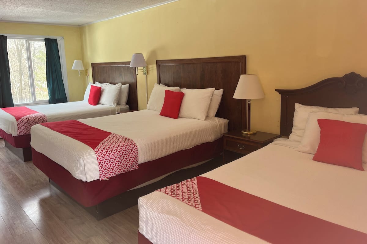 A hotel room with three beds, each with white bedding and red accents, wooden headboards, and bedside lamps.