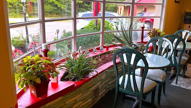 Ein Restaurant mit einer Steintheke, grünen Stühlen und Blick auf ein rotes Gebäude durch große Fenster.