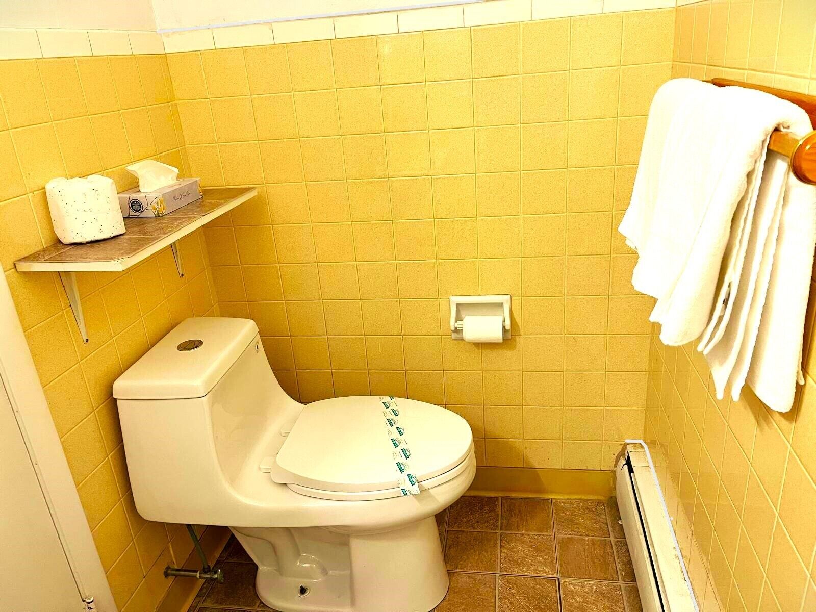 A small bathroom with a toilet, a shelf with toiletries, and a towel rack.