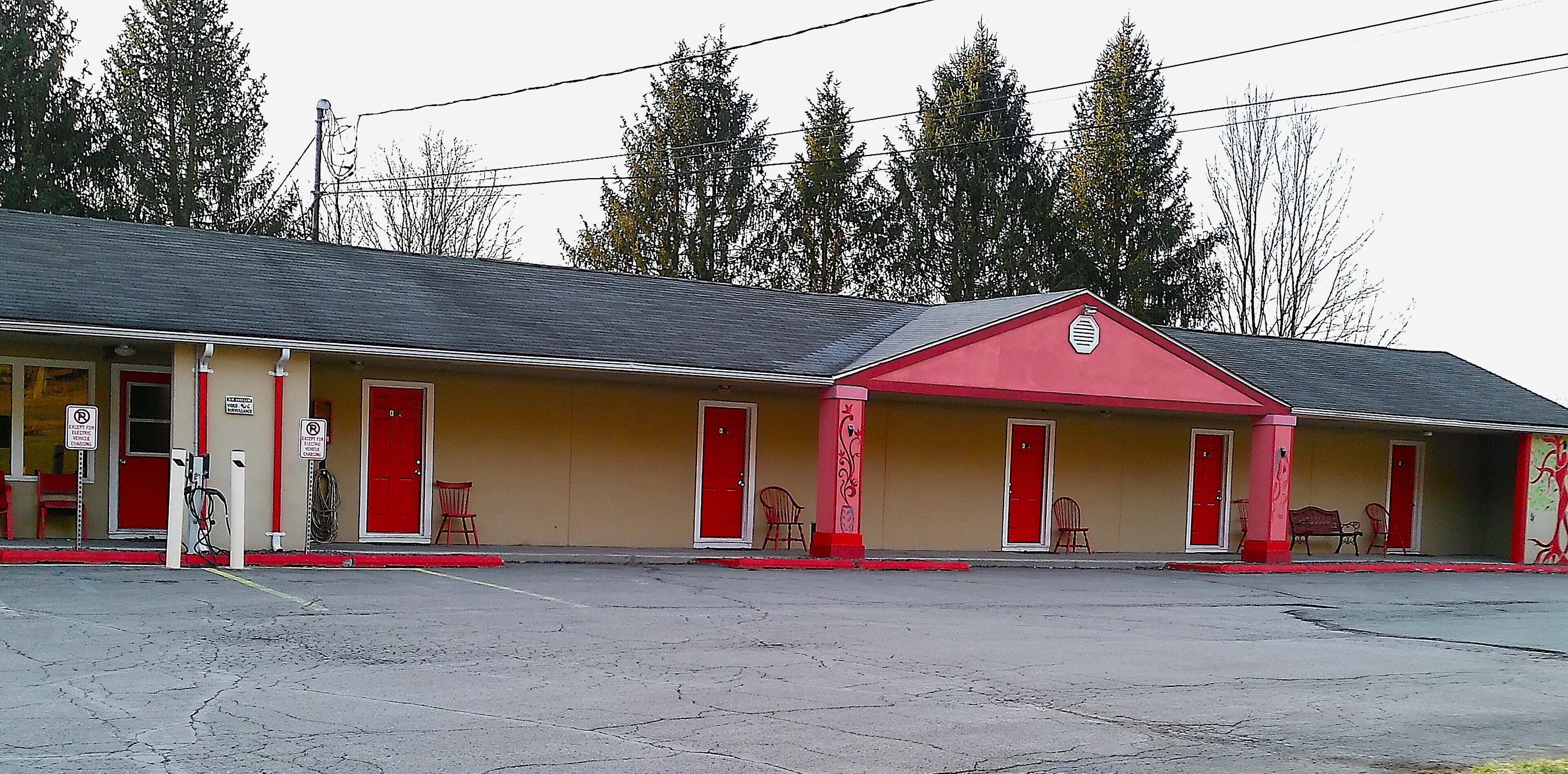 A motel with a red and beige facade, multiple red doors, and a parking lot in front.