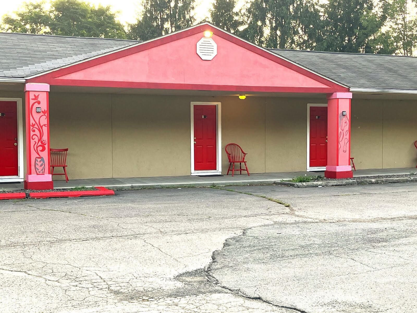 A building with a red facade and two red doors, each with a small porch area and a chair.