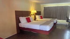 Ein Hotelzimmer mit zwei Betten, Holzboden, einem fenster mit Vorhängen und einem Schreibtisch mit Stuhl.