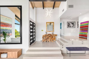 A modern interior with a staircase leading to a second floor, a wooden console table, a large mirror, and a colorful abstract painting. - Refreshed Mid-Century Retreat | Private Heated Pool, Spa, Steam & City Views (Los Angeles)