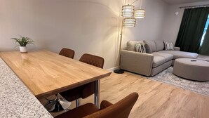 Een moderne woonkamer met een houten eettafel, bruine leren stoelen, een grijze bank en een vloerlamp.