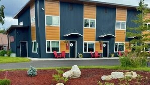A modern building with a two-story structure, featuring a mix of dark and light wood paneling, large windows, and outdoor seating with red chairs. - DWELL in Alaska "BIGGEST" Unit l (Fairbanks)