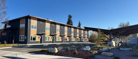A modern multi-story building with a flat roof, large windows, and a covered entrance area.