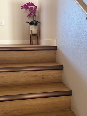 A wooden staircase with a dark edge trim, a potted orchid plant, and a wooden chair at the top.