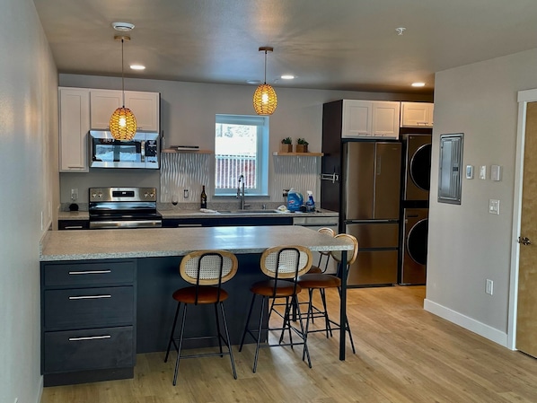 A modern kitchen with a central island, bar stools, stainless steel appliances, and pendant lighting.
