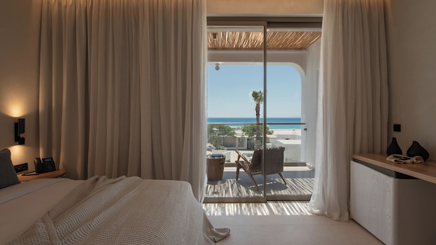 Een hotelkamer met een bed, een bureau, een stoel en een balkon met uitzicht op zee.