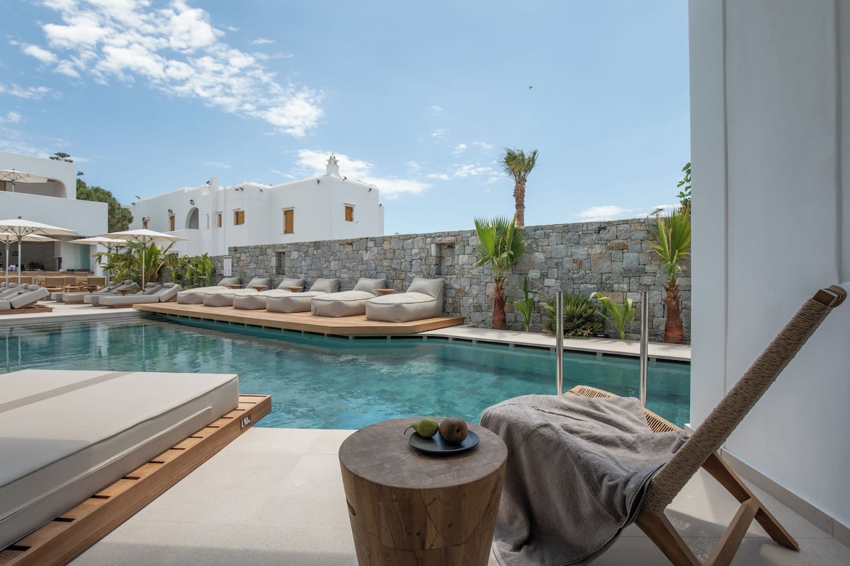 A poolside area with lounge chairs, a wooden table with fruit, and a stone wall.