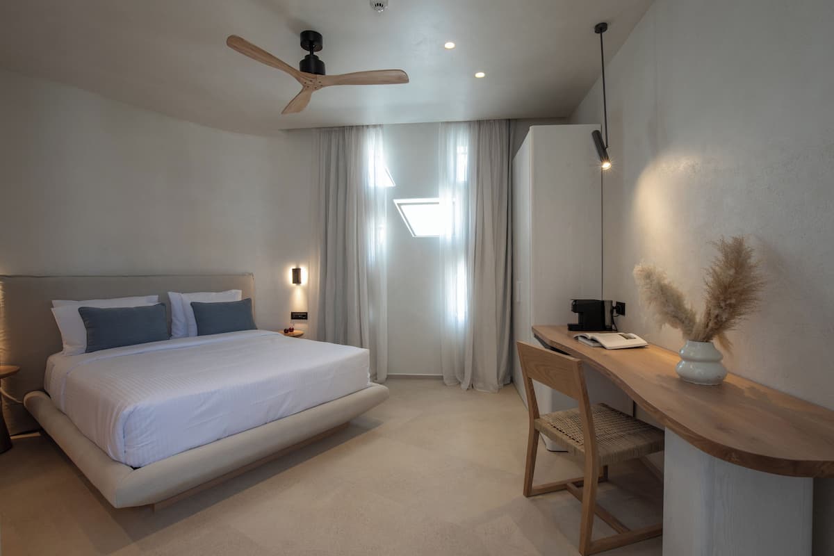 A modern bedroom with a large bed, a desk, and a ceiling fan.