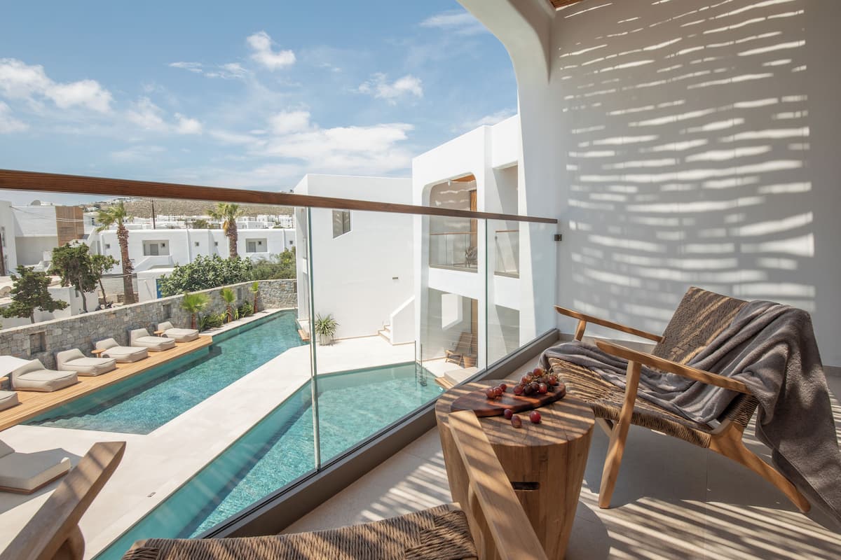 A modern balcony with a pool, wooden furniture, and a view of the surrounding buildings.