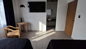 A room with two beds, a small table with a chair, a potted plant, a TV, and a bathroom visible through an open door. - Hotel Caminos (Chignahuapan)