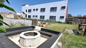 A modern building with multiple windows, a concrete fire pit, and a fenced yard. - Hotel Caminos (Chignahuapan)