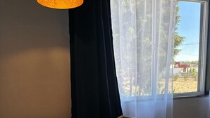 A room with a round wooden table, a wooden chair, a black pendant lamp, and a window with sheer curtains. - Hotel Caminos (Chignahuapan)