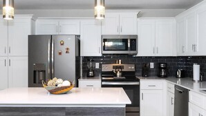 Une cuisine moderne avec des meubles blancs, des appareils en acier inoxydable et un îlot central doté de sièges.