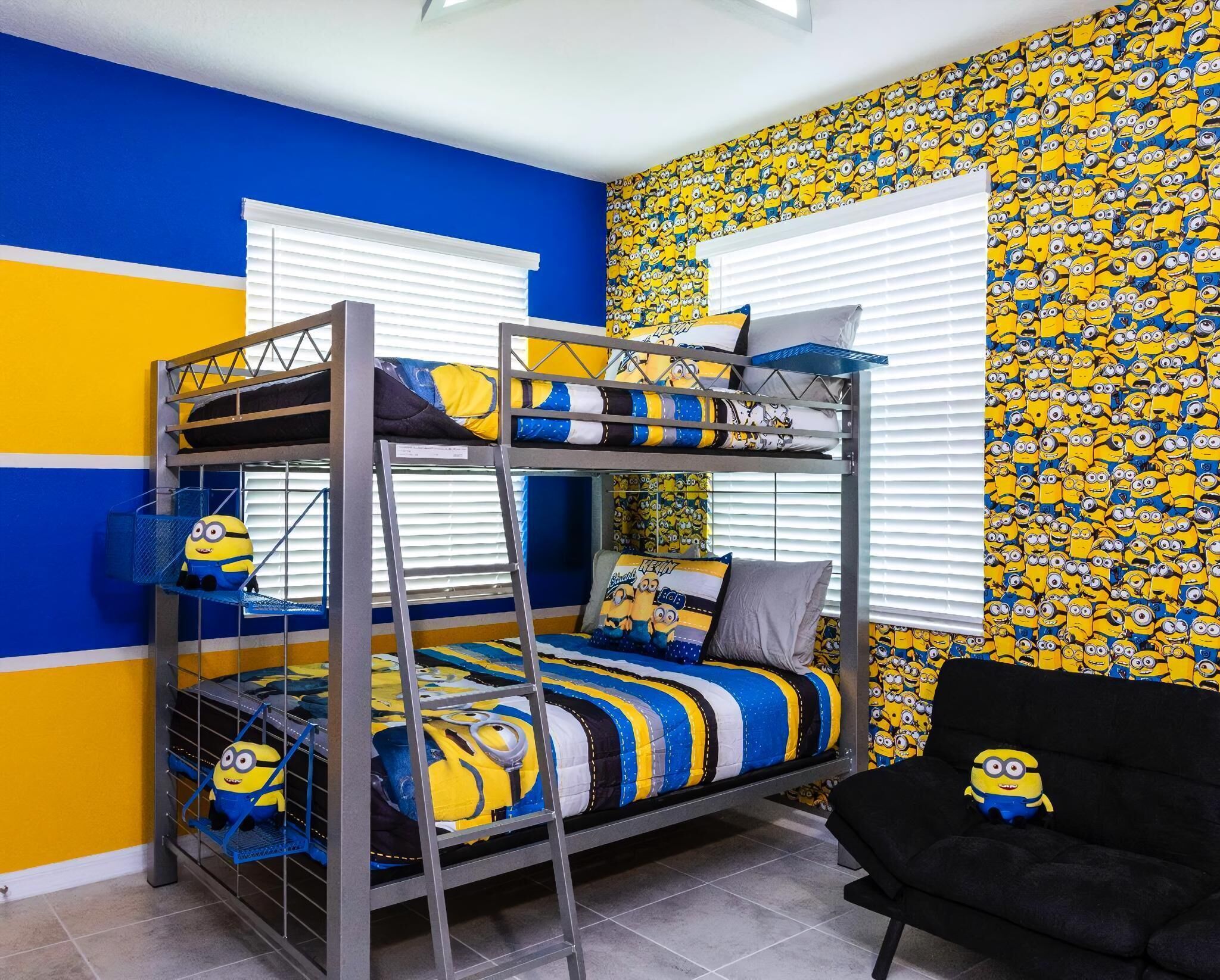 Un letto a castello con copriletto a tema Minions, un divano nero e una parete con carta da parati raffigurante i Minions.