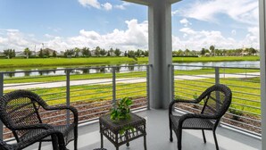 Un balcon avec deux fauteuils en osier et une petite table, donnant sur un champ verdoyant et une étendue d’eau.