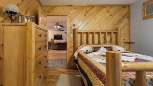 Une chambre à coucher en bois, avec un lit, une commode et un ventilateur de plafond.
