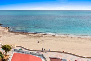 Een strand met een verharde promenade, een gebouw met een rood dak en een helder uitzicht op de zee.
