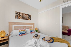 Een slaapkamer met een bed, kussens, een nachtkastje, een lamp, een dienblad met spullen en een hoed.