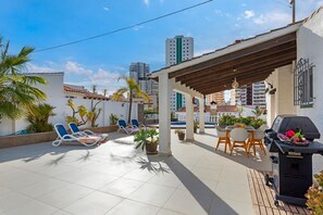 A rooftop patio with lounge chairs, a barbecue grill, and potted plants.