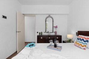 A hotel room with a bed, bedside table, dresser, mirror, and a door.